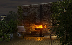 Der Gartenkamin von dyook brennt mit geöffneten Klappen. Der puristische Outdoor Kamin steht auf einer Dachterrasse vor einer Steinwand. Im Hintergrund sieht man ein erleuchtetes Hochhaus, es ist abends.
